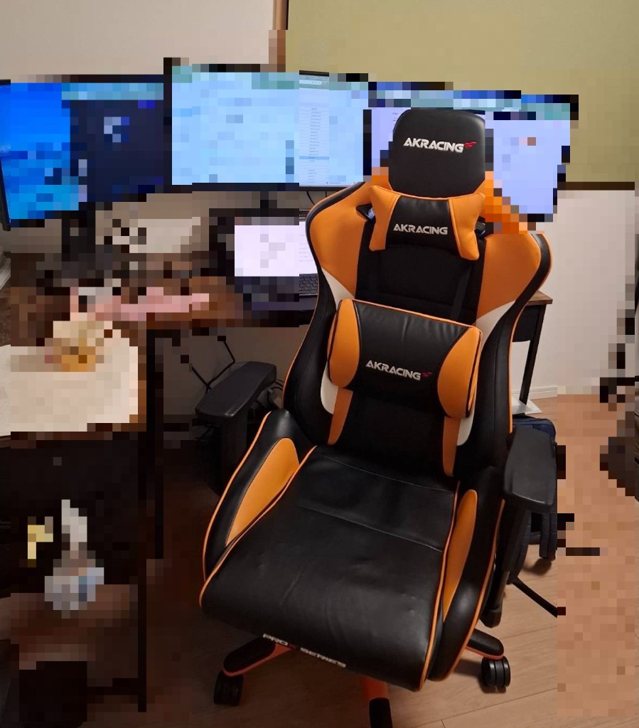 自宅のトリプルモニターデスクに設置した AKRacing Pro-X V2。黒とオレンジのゲーミングチェアがデスク環境に馴染んでいる様子