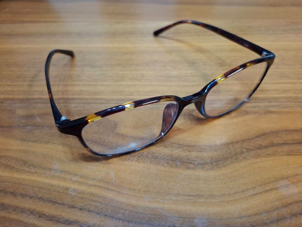 木目のデスクに置いた鼈甲柄のウェリントン型メガネ。ブルーライトカット用の眼鏡を斜めから撮影した様子