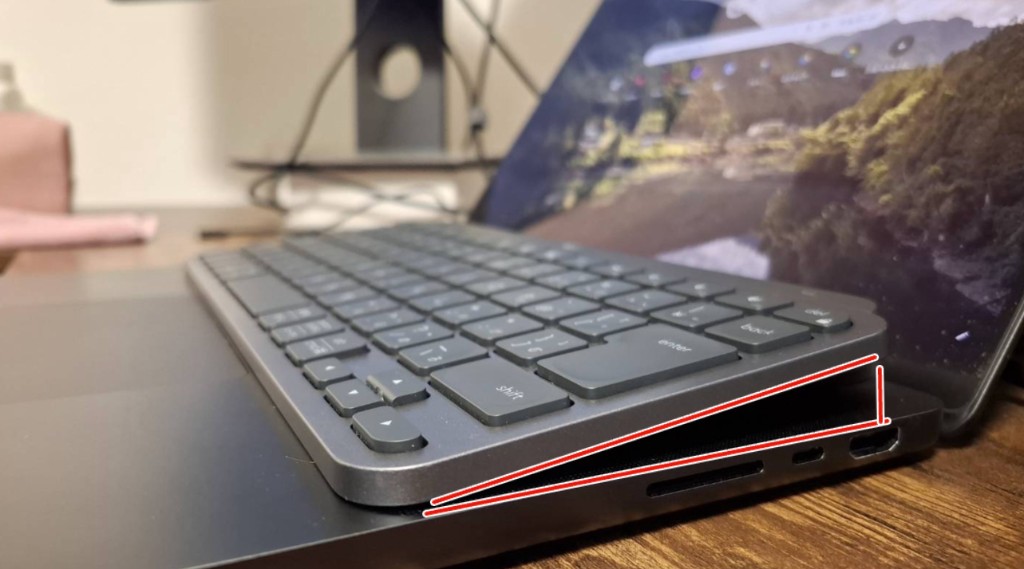 ノートPCのキー面の上に載せた MX Keys Mini の横から見た写真。キーボード背面側が少し持ち上がっており、赤い補助線で傾斜が示されている。トラックパッド側は空いている